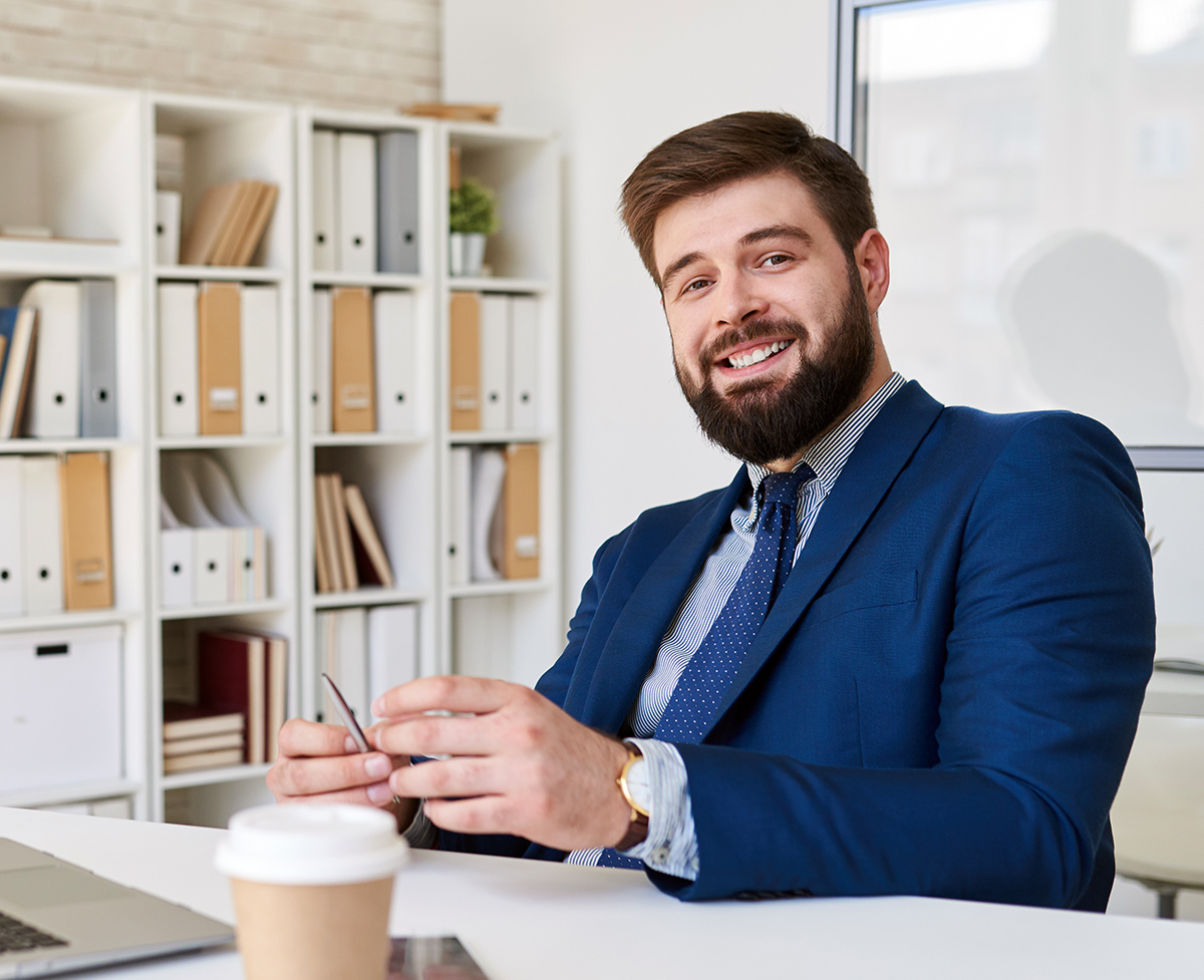 smiling-businessman-posing-at-desk-in-office-JTBMSTT.jpg
